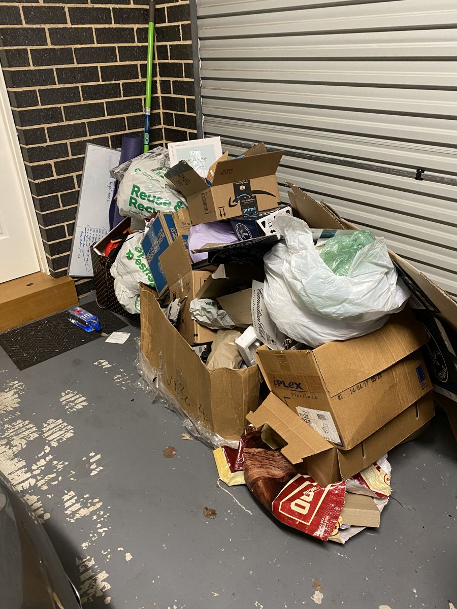 Pile of boxes and bagged rubbish stacked against a house wall before removal