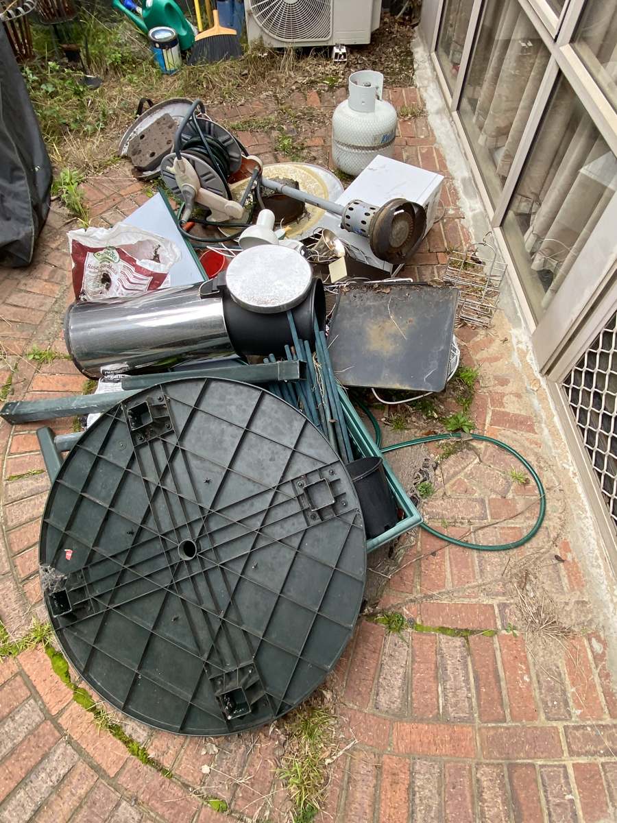 Old furniture, a table top and household junk piled in a backyard for collection