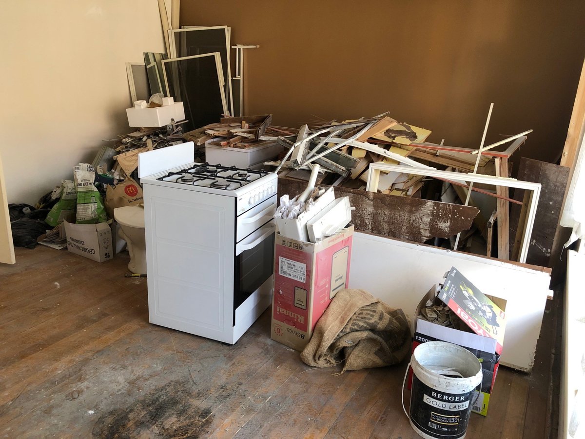 Stripped-out kitchen with an old oven, cabinetry and timber piled for removal